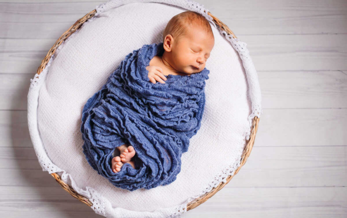 Newborn baby enveloped in blue scarf sleeps on white pillow